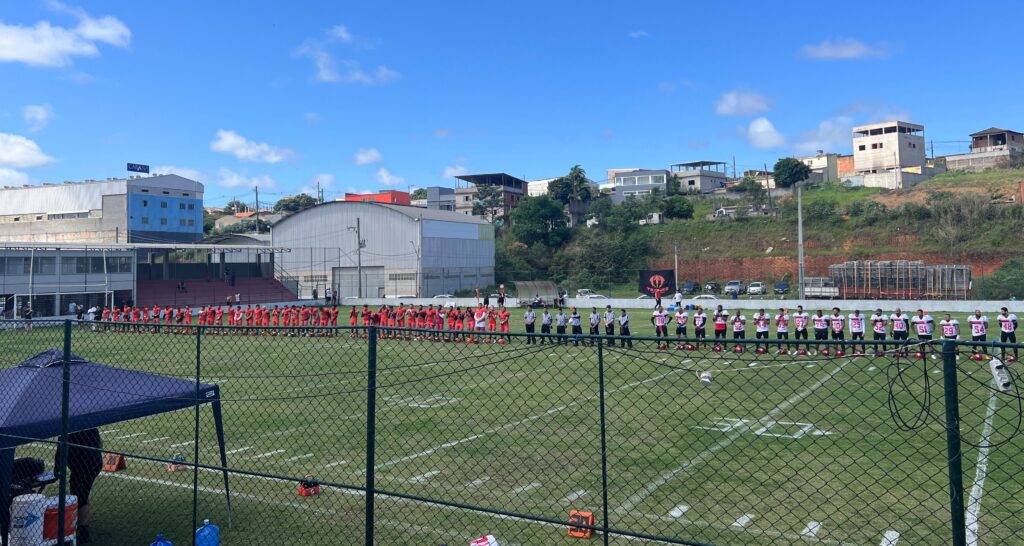 Foto de um campo de futebol americano em que duas equipes estão perfiladas lado a lado